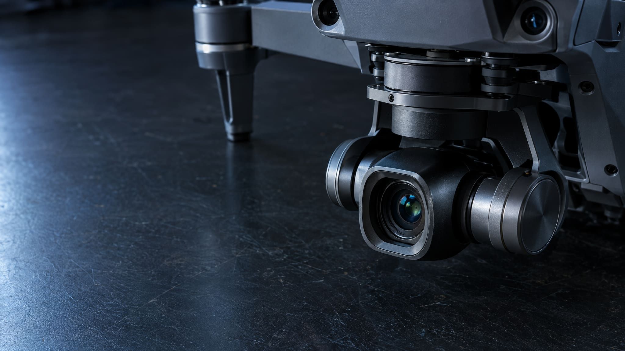 Macro detail of a gimbal and airframe on a dark workbench, cool directional light, calm space on the left